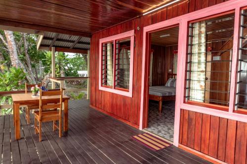 Leleana Resort Kolombangara Island的红色的房子,设有木甲板和桌子