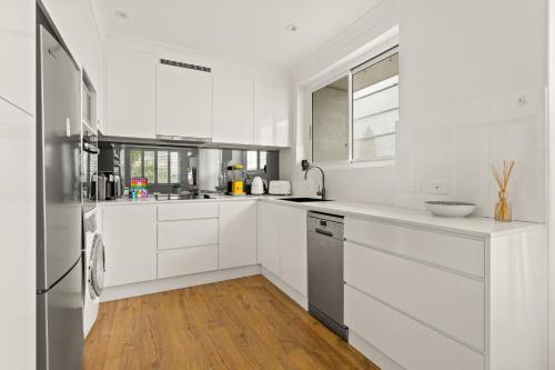 悉尼Chic apartment footsteps from Manly Beach的白色的厨房配有白色橱柜和木地板