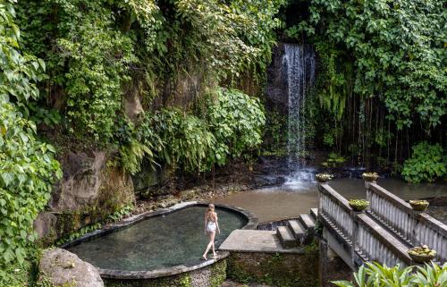 苏卡瓦提圣曼陀罗别墅及温泉酒店的站在瀑布前的游泳池中的女人