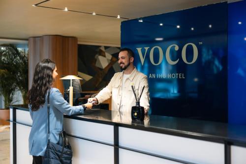 马德里voco Madrid Retiro, an IHG Hotel的女人在柜台上与男人握手