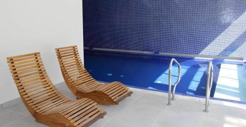 巴比松Les Pleiades Hôtel-Spa-Restaurant的两把木椅,坐在游泳池旁