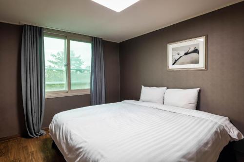济州市济州韩林姆肯辛顿度假酒店的卧室设有一张白色大床和一扇窗户。