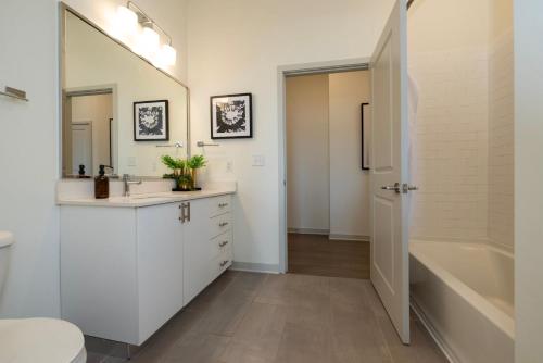 路易斯威尔Modern Nulu 2BR CozySuites 04的浴室配有白色橱柜、浴缸和水槽。