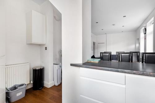 伦敦Spacious 2 bed Apartment with FREE PARKING for 2 cars and underground station Zone 2 for quick access to Central London up to 8 guests的厨房配有白色橱柜和带椅子的柜台。