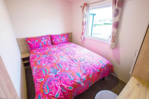 坎伯利SP158 - Camber Sands Holiday Park - 3 Bedrooms - Second Toilet - Decking - Private Parking的一个小房间,设有一张粉红色的床,配有窗户