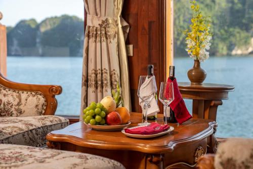下龙湾Emperor Cruises Legacy Ha Long的一张桌子,上面放着一碗水果和一瓶葡萄酒