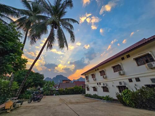 万荣Saphaothong guesthouse的落日后在一座建筑前的棕榈树