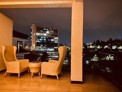 基加利AMORA APARTMENT的阳台上的三把椅子和一张桌子在晚上