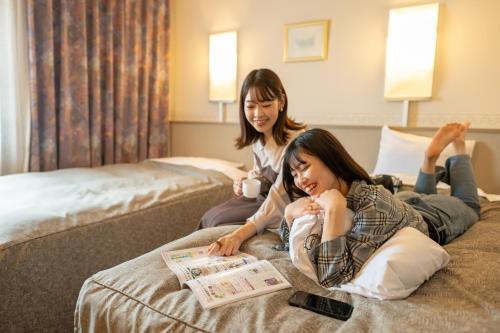 盛冈盛冈爱斯酒店的坐在床上看报纸的两名妇女