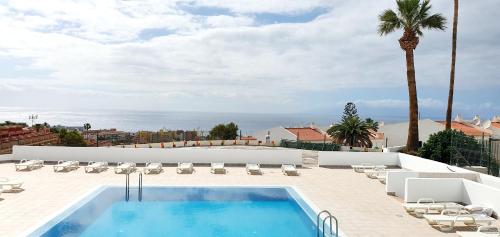 阿德耶Ocean View Apartments的一座带椅子和棕榈树的建筑屋顶上的游泳池