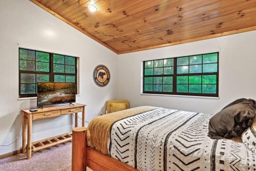 鸽子谷NEW HOT TUB! Secluded 3 Bed Cabin in Pigeon Forge的一间卧室配有一张床、一张书桌和两个窗户。