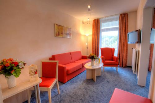 维林根Hotel Hochsauerland 2010的客厅配有红色的沙发和两把椅子
