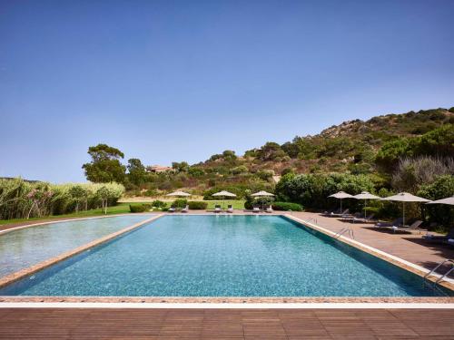 奇亚Baia Di Chia Resort Sardinia, Curio Collection By Hilton的一座带遮阳伞的游泳池,一座山底