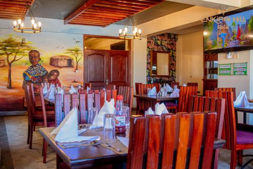 NarokEnkipai Hill Hotel的一间设有桌椅的餐厅,一名妇女站在后面