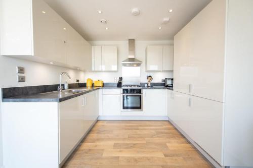 克劳利Modern 2 Bed Apartment in Crawley - Sleeps 5的厨房铺有木地板,配有白色橱柜。