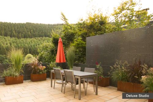 锡默拉特Rurtal de luxe的庭院配有桌椅和红色遮阳伞。