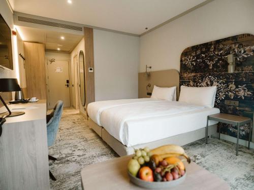 锡比乌Mercure Sibiu Arsenal的酒店客房,配有一张床和一碗水果放在桌子上