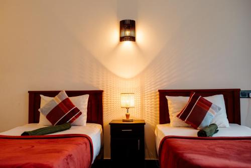 纳拉坦尼亚Adams Peak Inn的一间卧室设有两张床和一张桌子上的台灯。