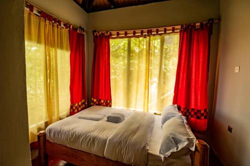 KapchorwaMise cave lodge的卧室配有红色窗帘,窗户前设有一张床