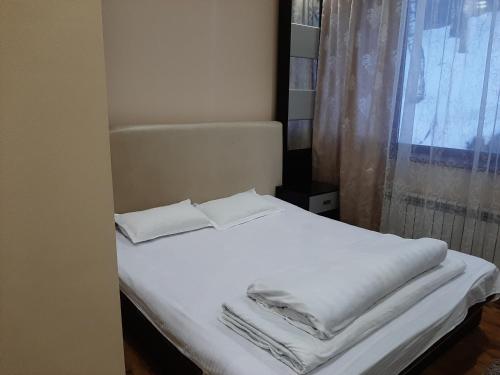 BesqaynarГостевой дом Almatau House的一张带白色床单和枕头的床以及窗户