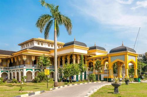 棉兰Danau Toba Hotel International的一座黄色的大建筑,前面有一棵棕榈树