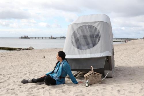 克伦胡森Schlafstrandkorb Nr 3的坐在帐篷旁边的海滩上的女人