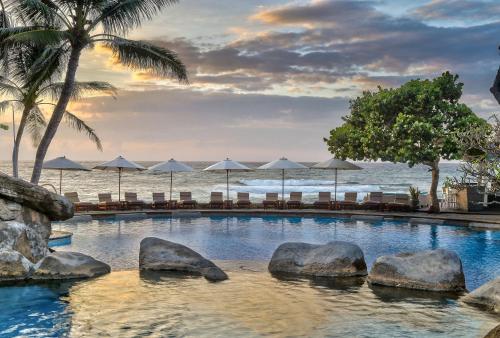 努沙杜瓦巴厘岛希尔顿度假村的毗邻大海的游泳池,配有椅子和遮阳伞