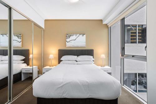 布里斯班Cosy 1-Bed Unit with a Gym, BBQ Area, Spa and Pool的卧室设有一张白色大床和两个窗户。