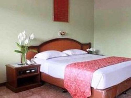 巴拉巴特Darma Agung Beach Hotel Parapat的一间卧室,配有一张床,桌子上放着花瓶