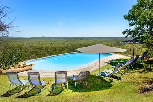 奥考奎约Etosha Safari Lodge, Etosha National Park, Namibia的一组椅子和一把遮阳伞,位于游泳池旁