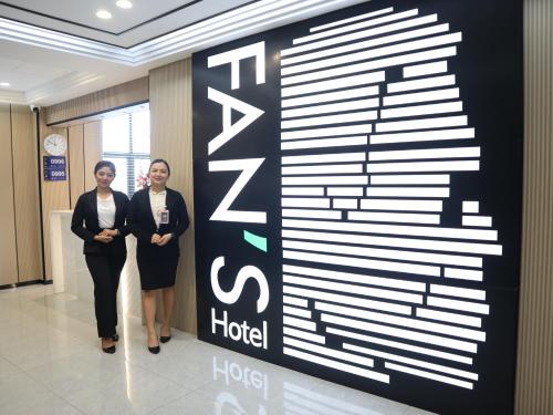 奥尔莫克Fan's Hotel- Ormoc的两个女人站在旅馆的一个标志旁