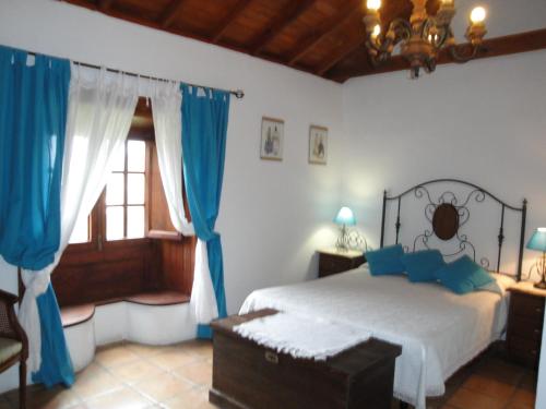 巴列埃尔莫索Casa Rural Guaidil的一间卧室配有一张带蓝色窗帘的床和一扇窗户