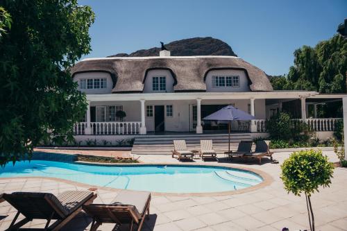 弗朗斯胡克Mirabelle Guesthouse的茅草屋顶和游泳池的房子