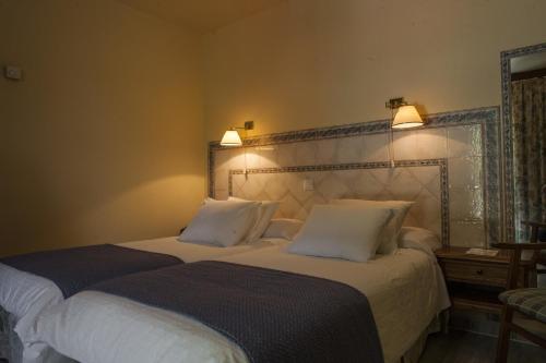 AlcedaHotel Balneario De Alceda的卧室内的两张床,墙上有两盏灯