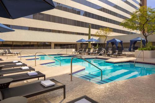凤凰城凤凰凯悦酒店的一座带椅子和遮阳伞的游泳池位于一座建筑旁边