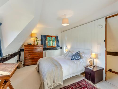 Malting Cottage的卧室配有白色的床和木制梳妆台。