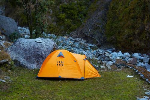 达兰萨拉Bal Camps by Hike House的岩石旁的草上有一个橙色的帐篷