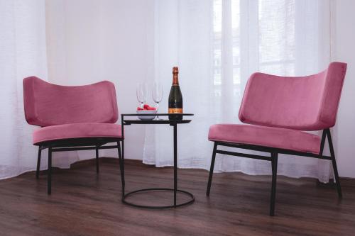 的里雅斯特Residence Piazza Giotti 8的两张粉红色的椅子和一张桌子上的一瓶葡萄酒