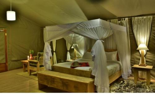 SekenaniDan Maasai Mara safari camp的一间卧室配有一张天蓬床,内设长凳