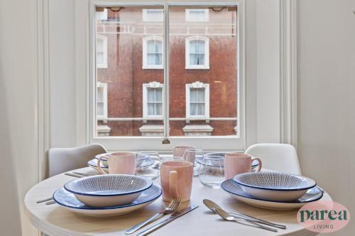 伦敦Parea Living - South Kensington, Elegant 1-Bedroom Flat, WFH Desk的餐桌,餐桌上摆放着盘子和银器,窗户上摆放着