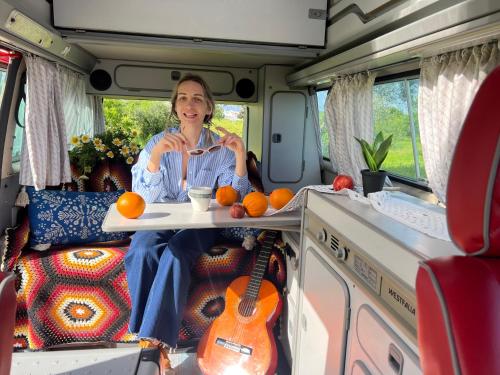波尔蒂芒Rent a Blue Classics' s Campervan for your Road trip in Portimao -VOLKSWAGEN T3的坐在面包车后面的女士,带上一盘橙子