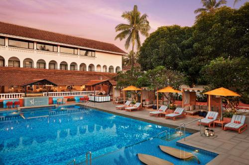卡兰古特Ronil Goa - a JdV by Hyatt Hotel的一座带椅子和遮阳伞的游泳池位于一座建筑旁边