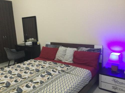 富查伊拉1 bedroom apartment的一间卧室配有一张带红色枕头的床和紫色灯