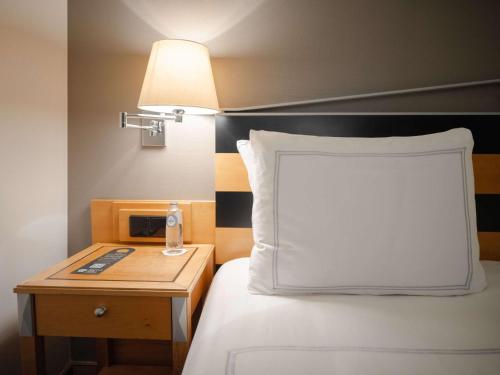 阿姆斯特丹瑞士酒店的一张带白色枕头的床和一个带灯的床头柜