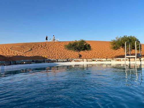 梅尔祖卡Sahara Majestic Luxury Camp的一座水池,人们站在山丘上