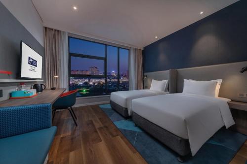 开封开封迪臣智选假日酒店的酒店客房设有两张床、一张书桌和一个窗户。