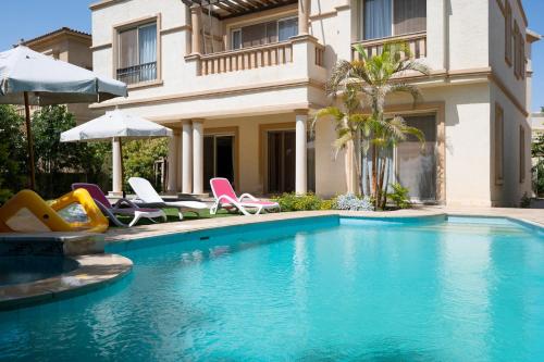 开罗Zyra Luxury villa with pool and Jacuzzi in New Cairo的房屋旁的游泳池配有椅子和遮阳伞