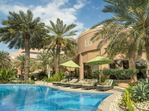 麦纳麦巴林瑞享酒店的一个带椅子和棕榈树的度假游泳池