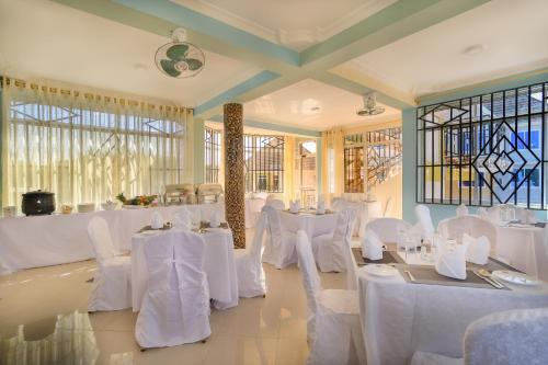 MbuguniNew Mazubu Grand Hotel Mererani的配有白色桌椅和窗户的客房
