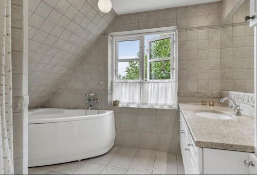 HøjbjergNyere villa nær by, skov, strand的带浴缸、两个盥洗盆和窗户的浴室